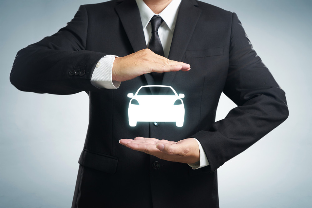 Car (automobile) insurance and collision damage waiver concepts. Businessman with protective gesture and icon of car. Wide banner composition and bokeh in background.
