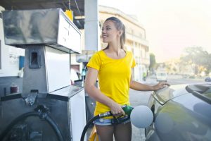woman wearing a yellow shirt and denim shorts refueling a sleek, modern car